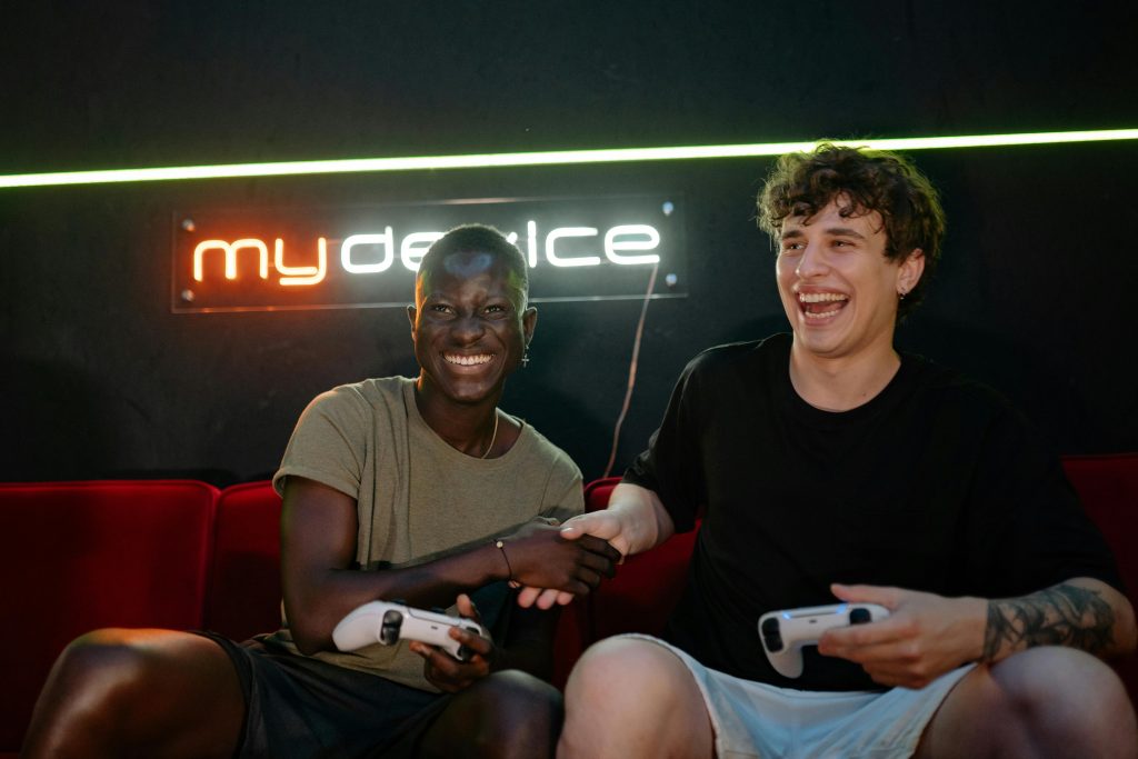 Two cheerful friends playing video games and shaking hands on a couch.