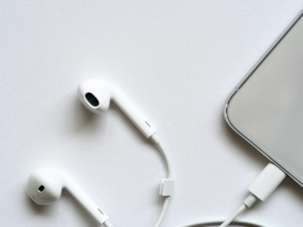 Minimalist top view of white wired earphones connected to a smartphone on a clean white background.